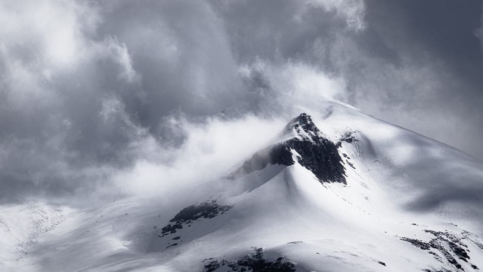 Snowy mountain summit wrapped in dramatic clouds